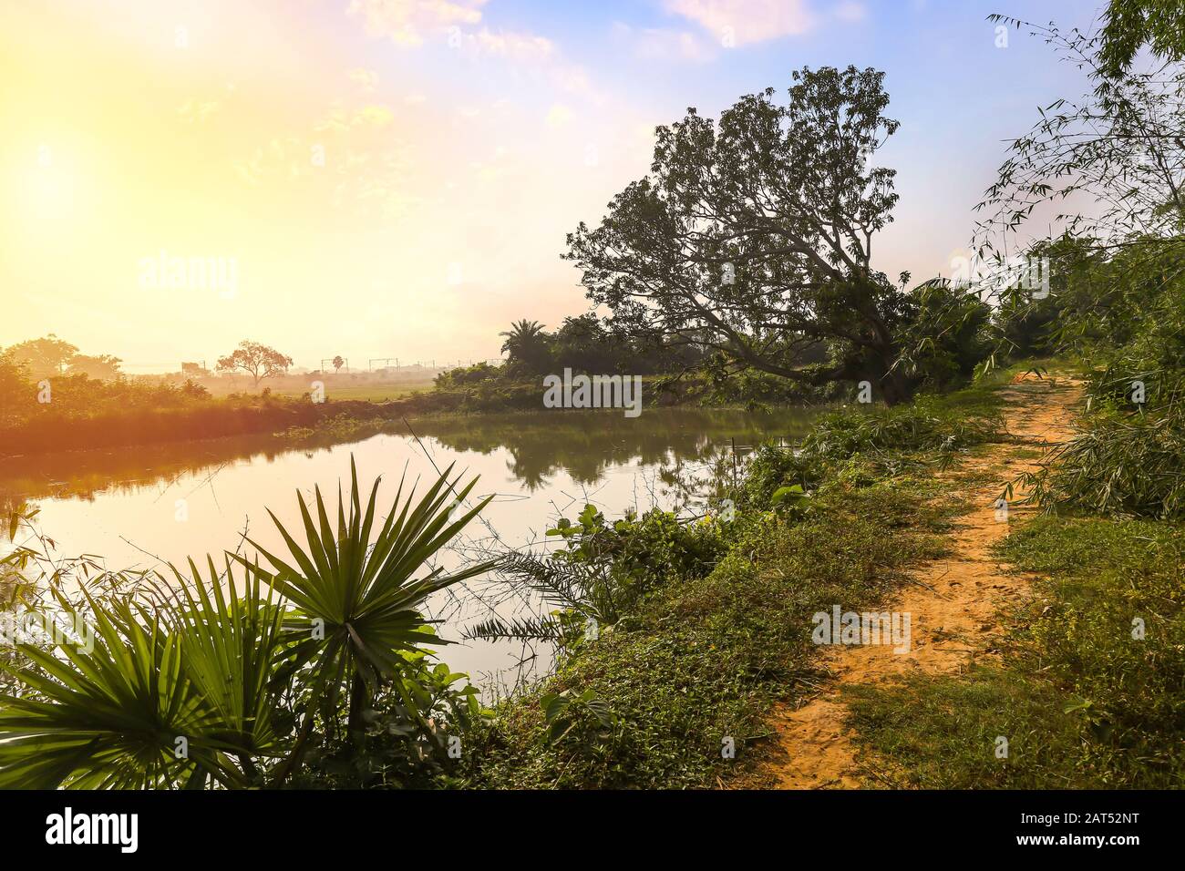 Ländliche Landschaft in Indien mit unbefestigter Dorfstraße und Teich bei Sonnenaufgang Stockfoto