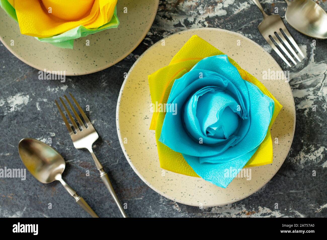 Dekorative Blume aus farbigen Papierservietten. Tischeinstellung mit farbigen Papierservietten auf Steingrund, flacher Lay. Stockfoto