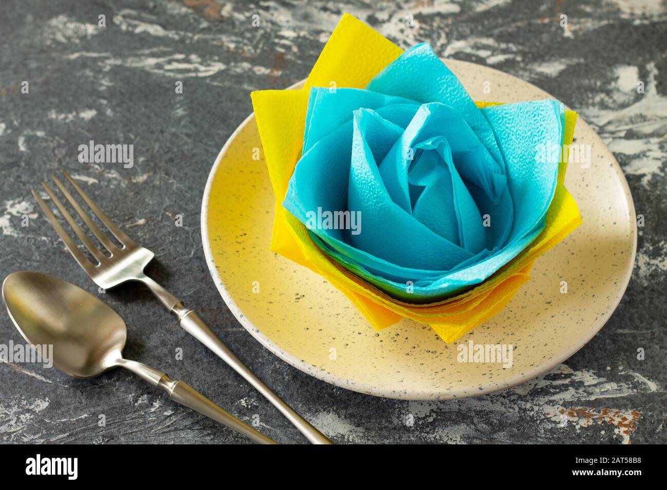 Dekorative Blume aus farbigen Papierservietten. Tischeinstellung mit farbigen Papierservietten auf Steinhintergrund. Freier Speicherplatz für Ihren Text. Stockfoto