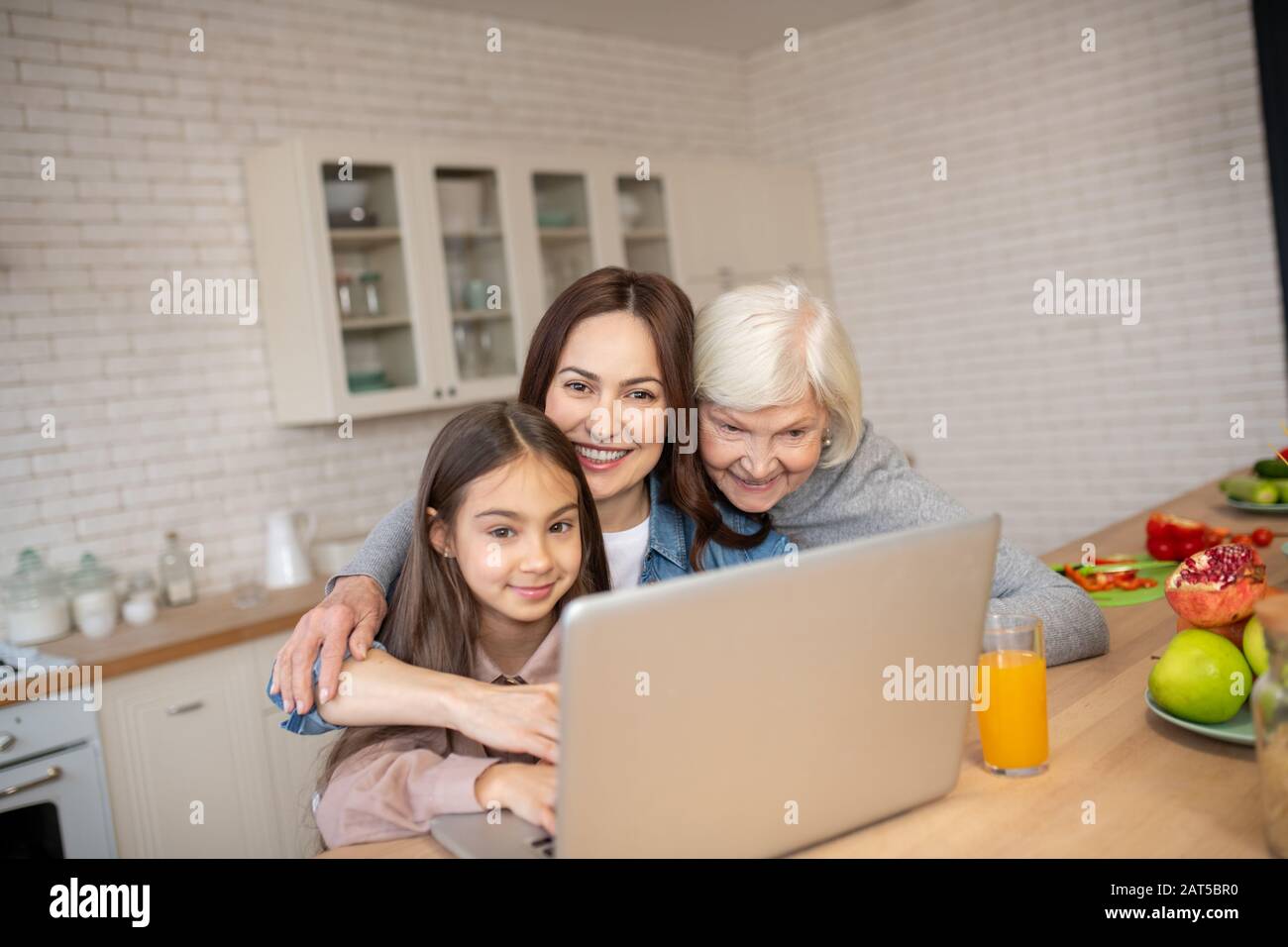 Großmutter, Mutter, Tochter umarmte sich an einem Laptop in der Küche. Stockfoto