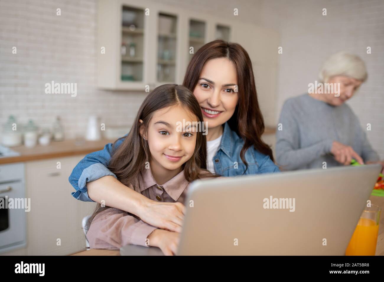 Glückliche Mutter mit Tochter in der Nähe von Laptop und Großmutter. Stockfoto