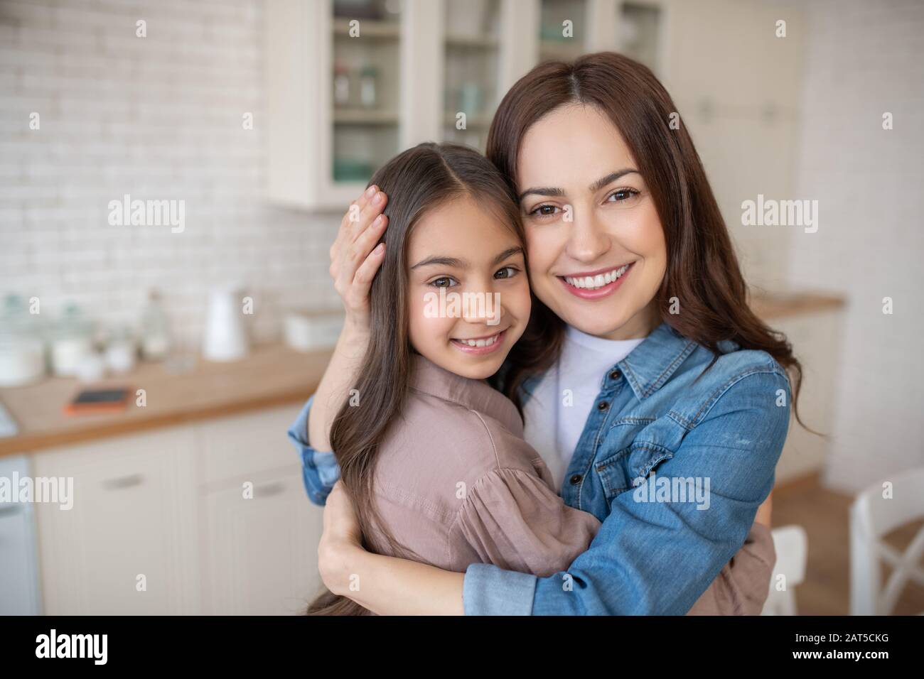 Liebevolle junge Mutter umarmt ihre kleine Tochter. Stockfoto