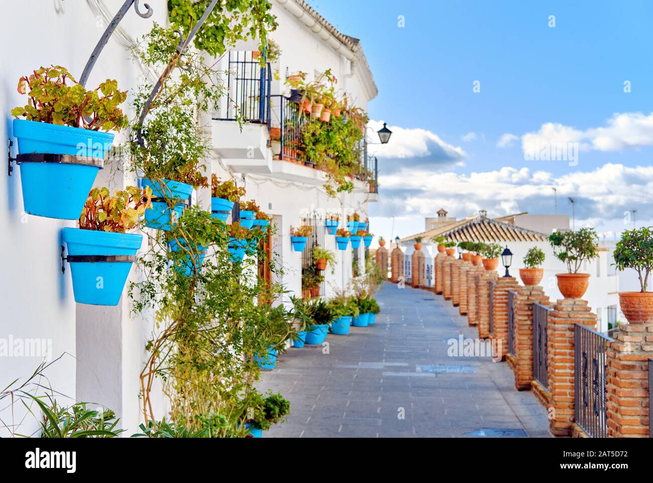 Idyllische Landschaft leere malerische Straße des kleinen weiß gewaschenen Dorfes Mijas. Pfad dekoriert mit hängenden Pflanzen in hellblauen Blumentöpfen Spanien Stockfoto