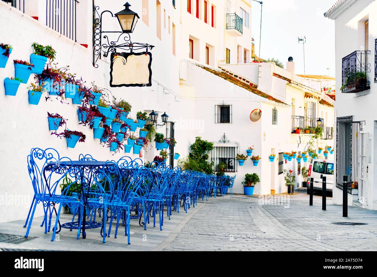 Mijas Pueblo Blanco, charmantes kleines Dorf, malerische leere Straße in der Altstadt mit hellblauen Tischen Stühle des lokalen Cafés, Blumentöpfe hängen an Stockfoto