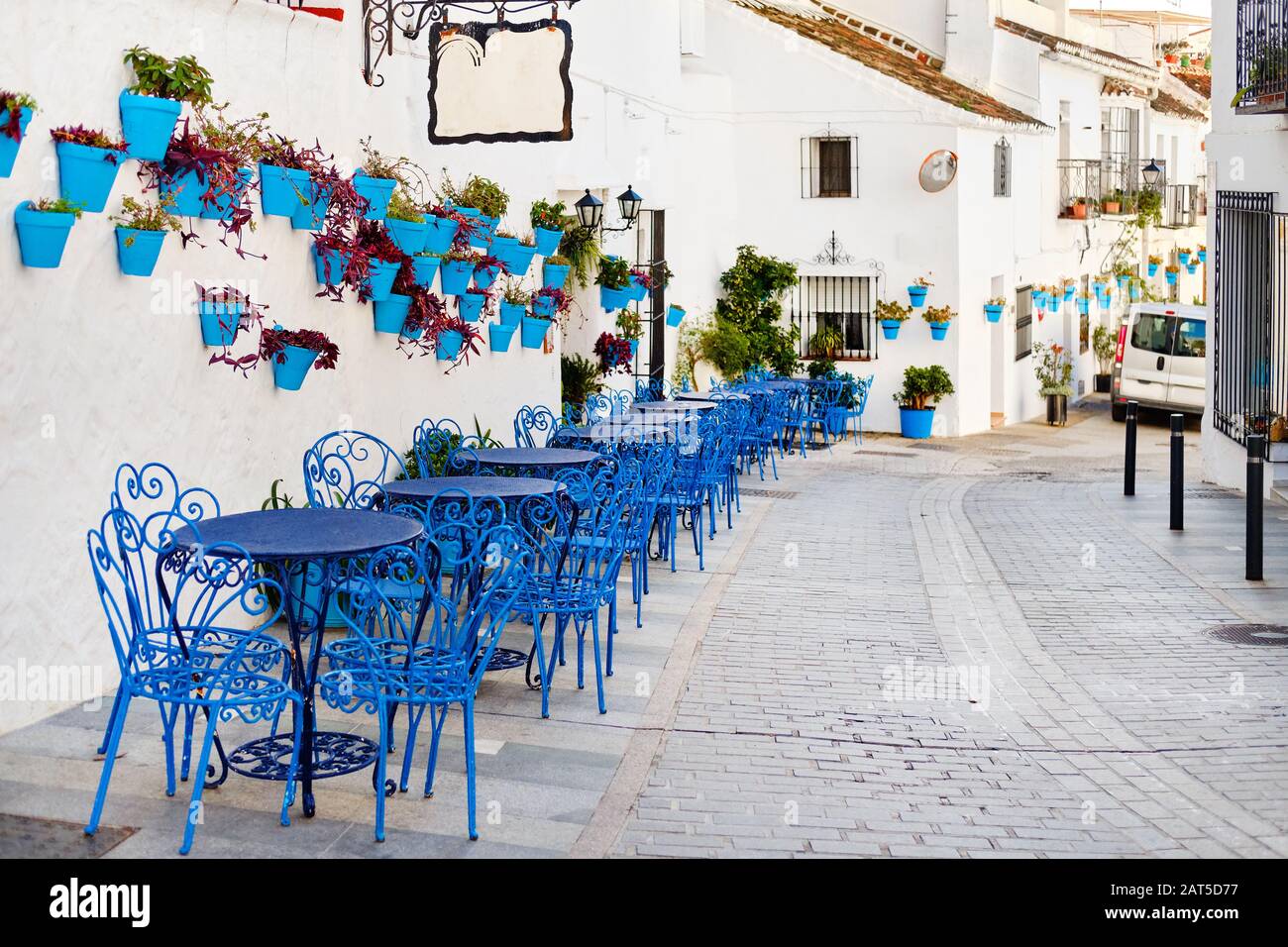 Mijas Pueblo Blanco, charmantes kleines Dorf, malerische leere Straße in der Altstadt mit hellblauen Tischen Stühle des lokalen Cafés, Blumentöpfe hängen an Stockfoto