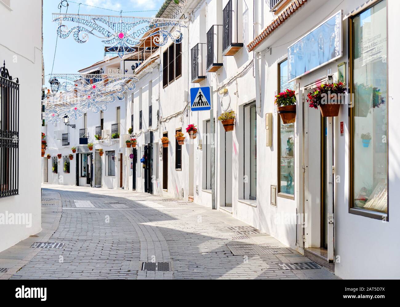 Mijas weiße Straße, kleines berühmtes Dorf in Spanien. Charmante, leere Gassen mit Neujahrsdekorationen, an den Wänden hängen Blumentöpfe Stockfoto