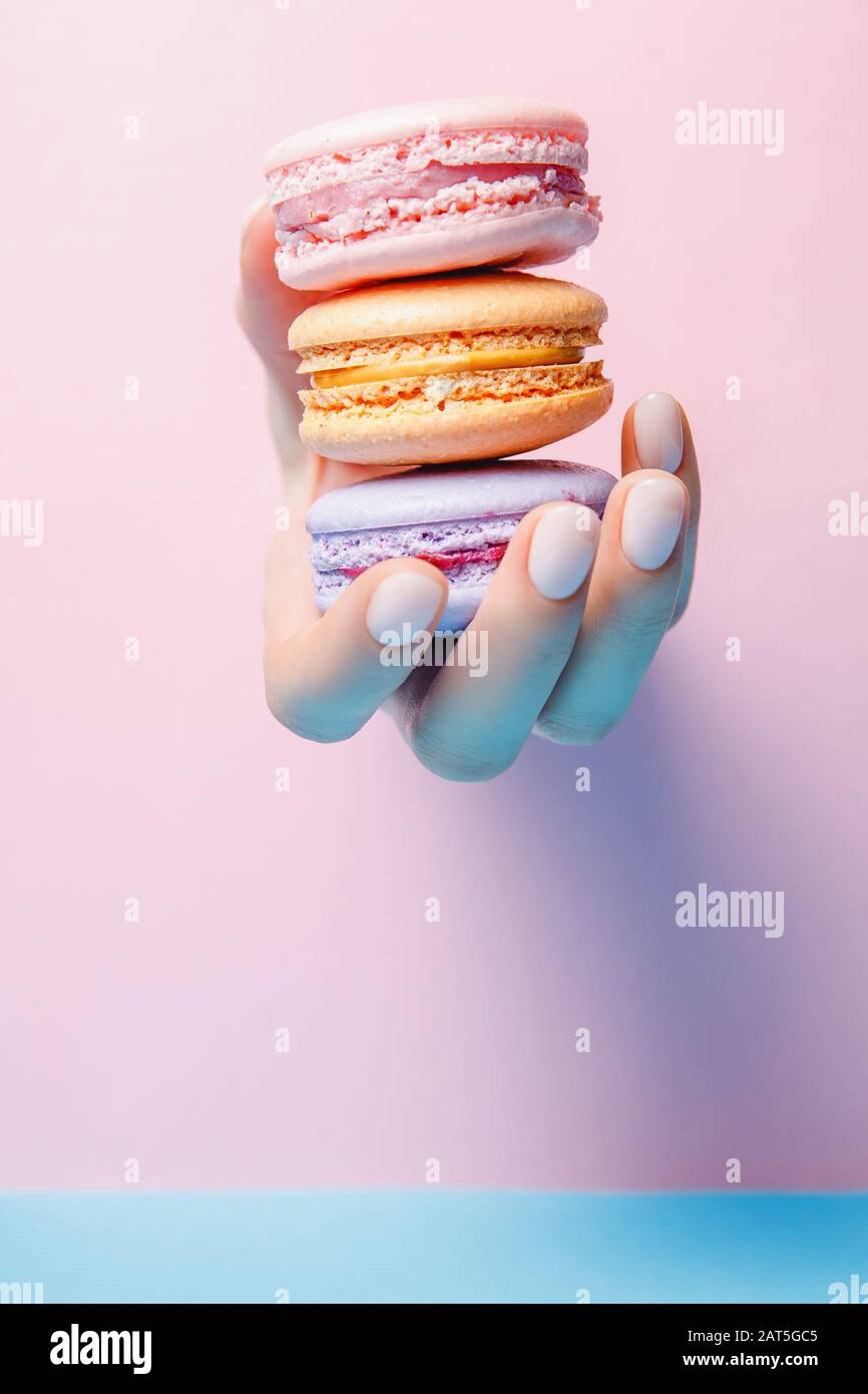 Beauty Hand Mädchen mit modischer Maniküre, die farbige Makronen auf pinkfarbenem und blauem Hintergrund nimmt Stockfoto