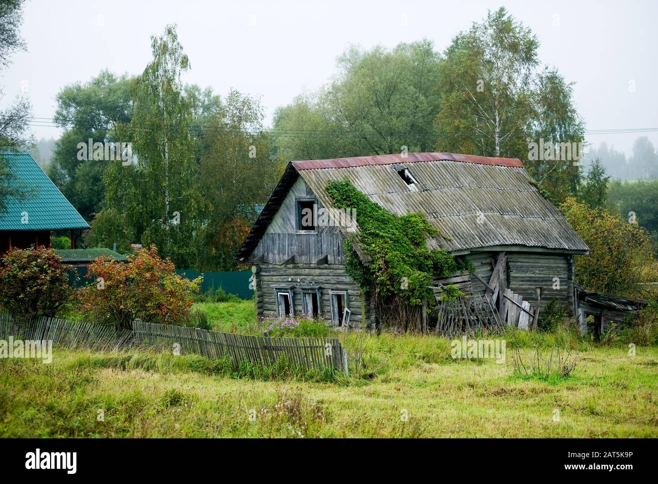 Altes verlassenes, unschickes altes Holzhaus ohne Fenster mit einem teilweise fehlenden Zaun in einem entfernten Dorf. Stockfoto