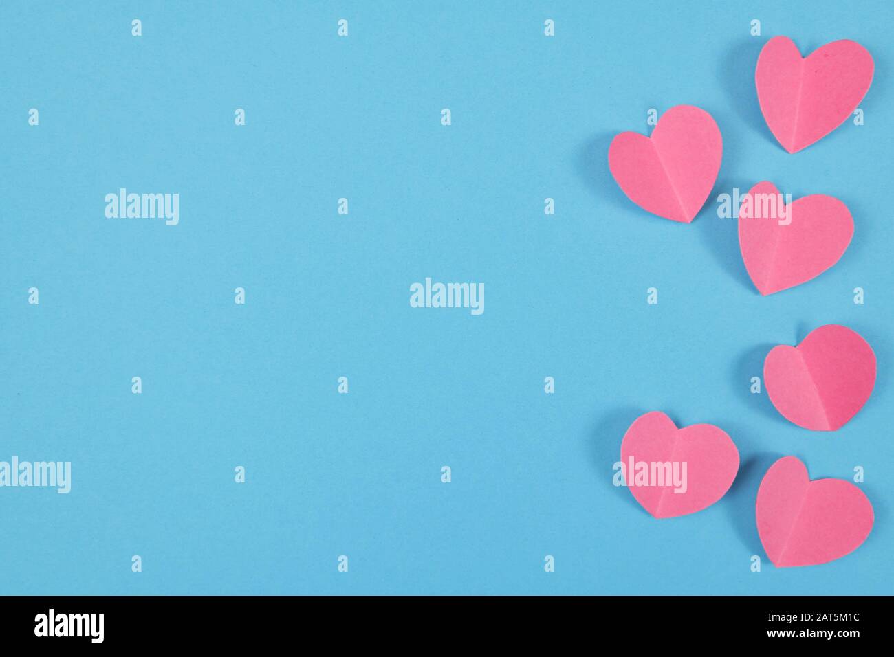 Blauer Valentinhintergrund mit niedlichen pinkfarbenen Papierherzen auf der rechten Seite und leerem Kopierbereich auf der linken Seite Stockfoto