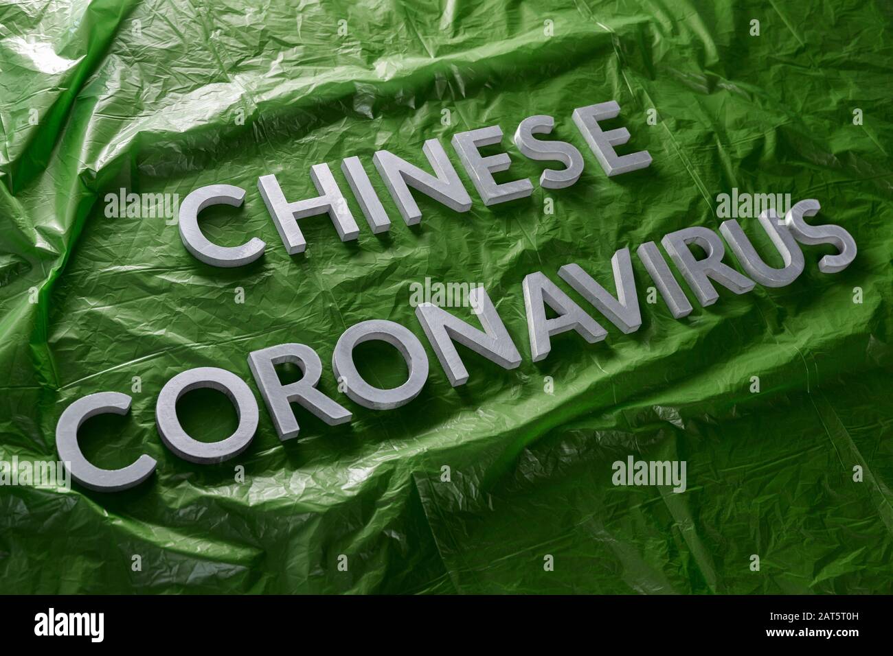 Die Wörter chinesisches Coronavirus wurden mit silbernen Metallbuchstaben auf gelegt Grün zerknitterte Plastikfolie - diagonale Zusammensetzung Stockfoto