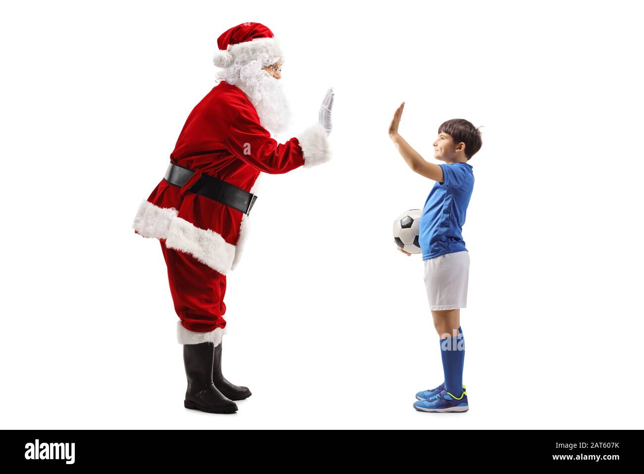 Lange Profilaufnahme des Weihnachtsmannes, der mit einem Jungen in einem Fußballoutfit, isoliert auf weißem Hintergrund, hohe fünf Gesting Stockfoto