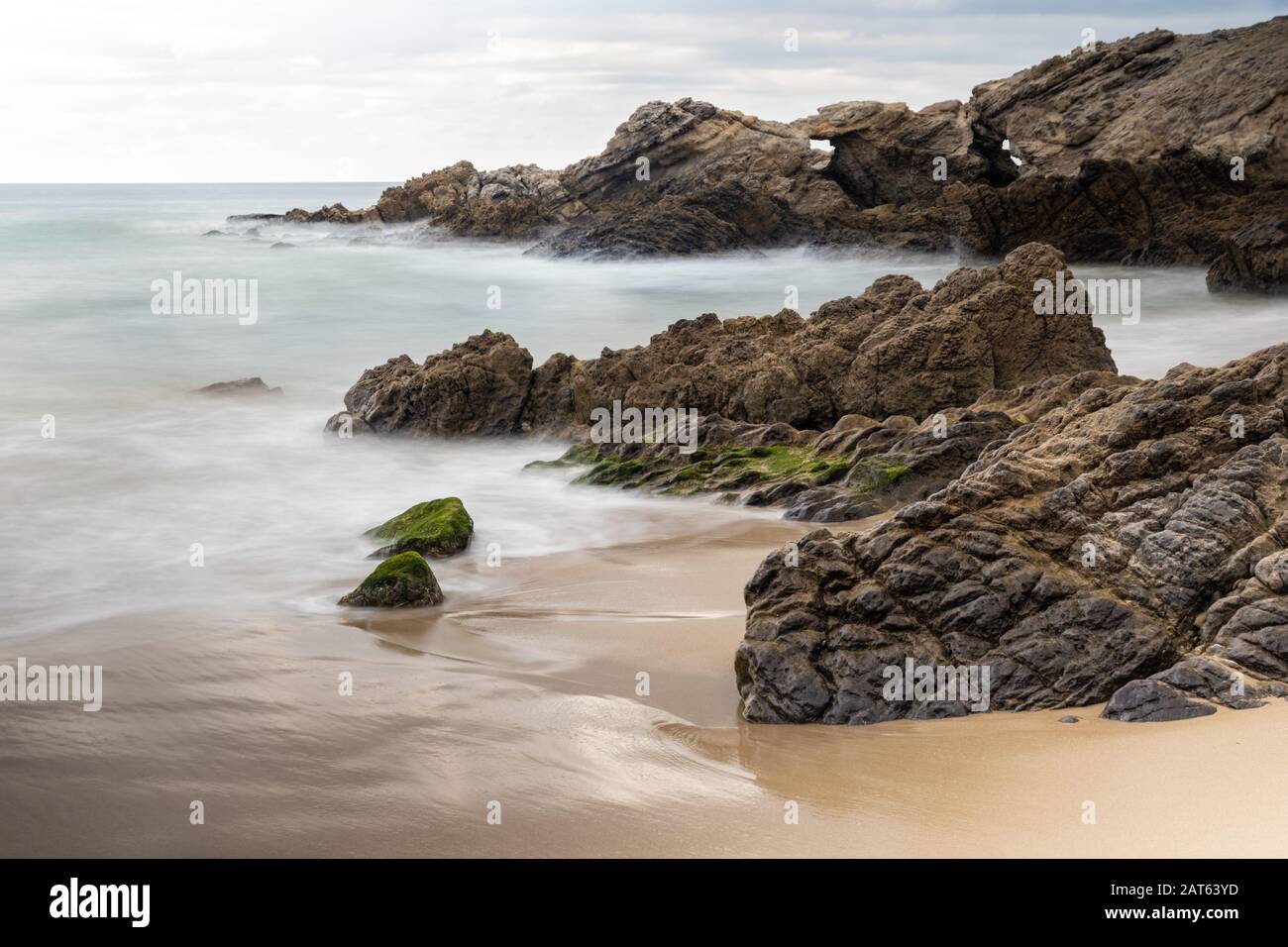 Leo Carrillo Beach in der Nähe von Malibu, Kalifornien. Zerklüftete Küstenfelsen; glatter brauner Strandsand; seidiger Ozean darüber hinaus. Bewölkt oben. Stockfoto