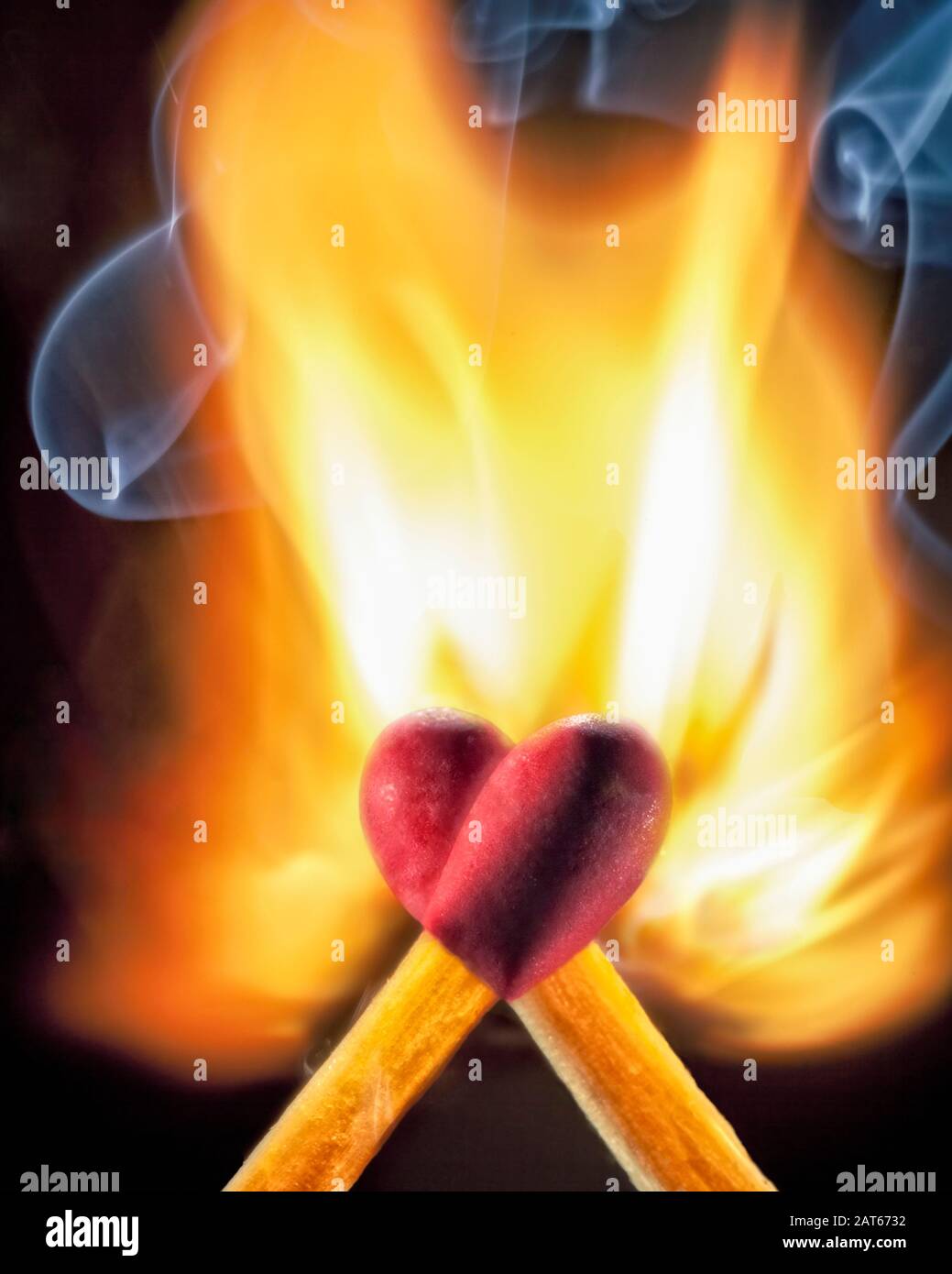 Zwei Holzmatchstöcke mit roten Spitzen überlagern sich, um eine Herzform zu bilden, während sie sich in Flammen entzünden Stockfoto