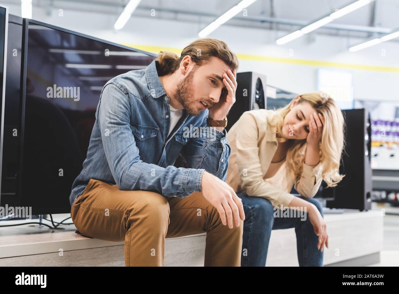Trauriger Freund und Freundin sitzen in der Nähe des neuen fernsehers im Haushaltsgerätgeschäft Stockfoto