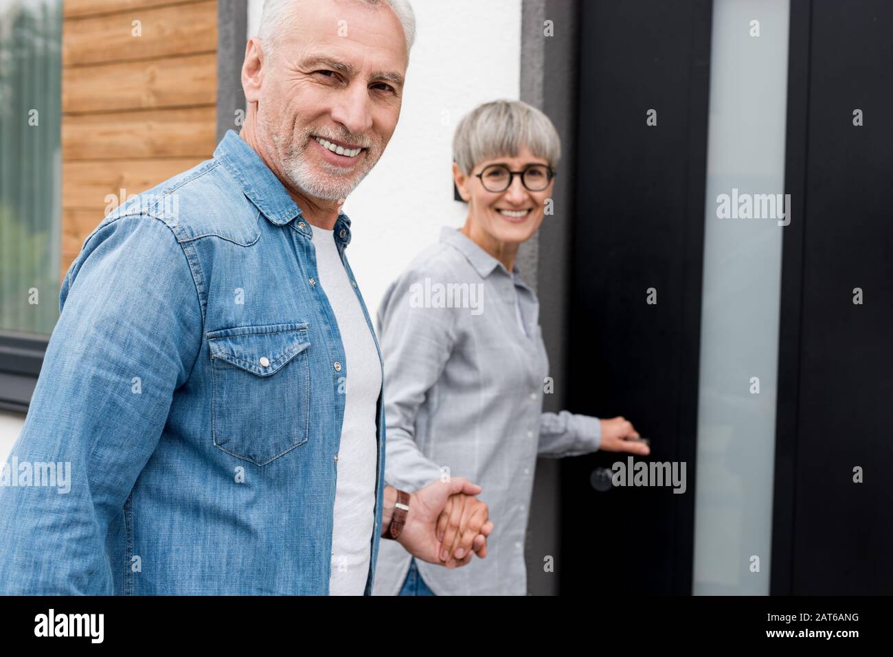 Lächelnde Frau, die die Hände mit dem Mann hält und in ein neues Haus eindringt Stockfoto