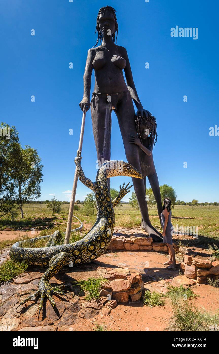Eine Besucherin, die ein Gefühl von Ausmaßung gibt, während sie die Statue einer Mutter, eines Kindes und einer Goanna von Anmatjere bei Einem Querruder im Northern Territory bewundert. Stockfoto