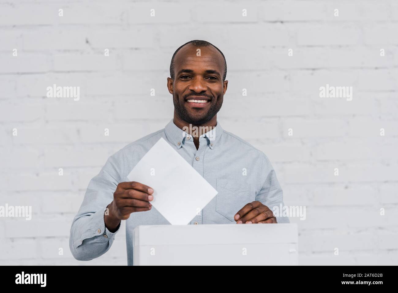 Glückliche afroamerikanische Wähler, die leere Stimmzettel in die Wahlbox stellen Stockfoto