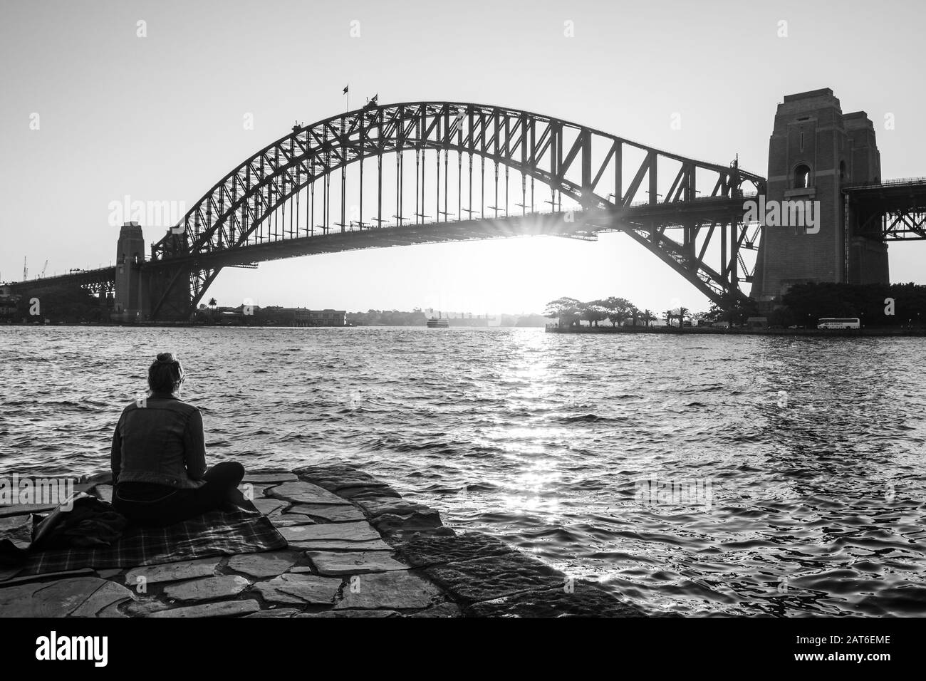 Dame, die über den Sonnenuntergang hinter der Hafenbrücke nachdenkt Stockfoto
