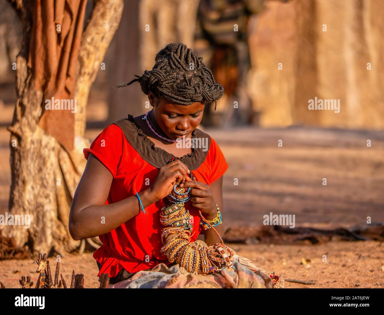 Ländliches Namibia - 21. August 2016. Eine junge Frau in einem Himba-Stammesdorf, die sich darauf vorbereitet, Handwerk an Touristen zu verkaufen, was eine wichtige Einnahmequelle ist. Stockfoto
