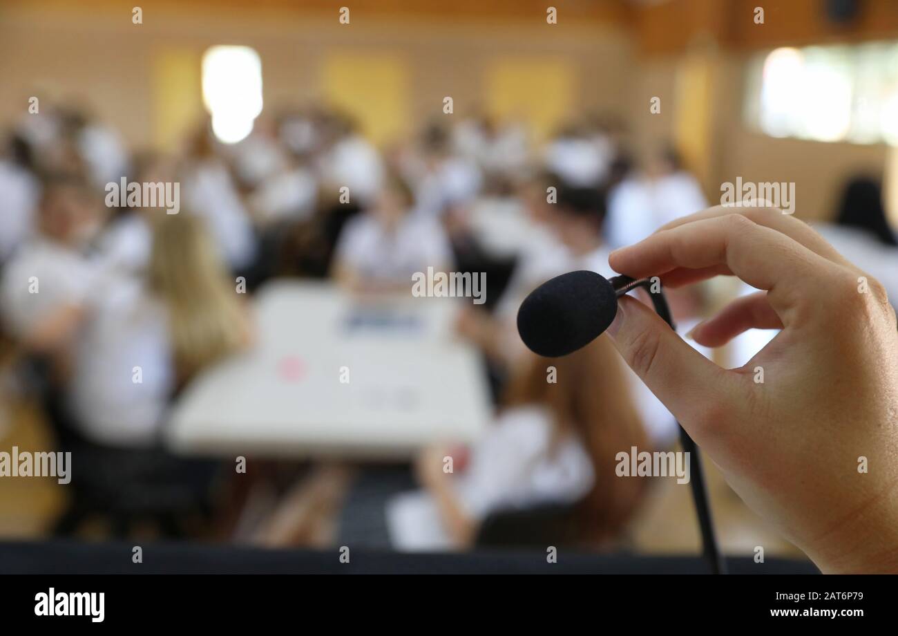 Ein Sichtbild einer Hand und Finger, die ein Mikrofon halten und einstellen, während sie in der Öffentlichkeit vor einem Publikum in einem Saal sprechen Stockfoto