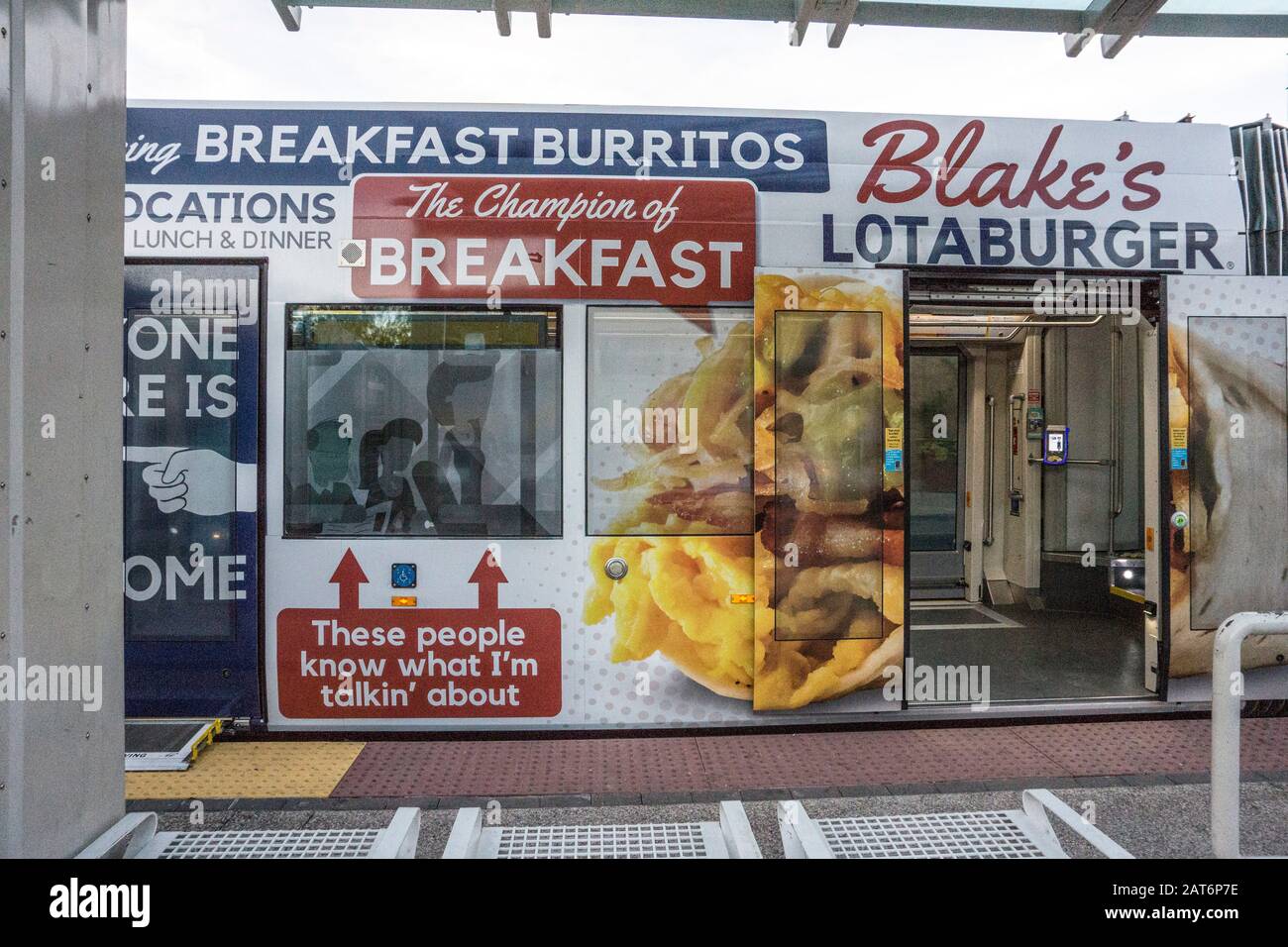 Sun Link Straßenbahn teilweise gesehen angehalten im Schutzraum mit Türen offen & Auto außen mit amüsanter Übergröße Werbung für Frühstück burritos gestrichen Stockfoto