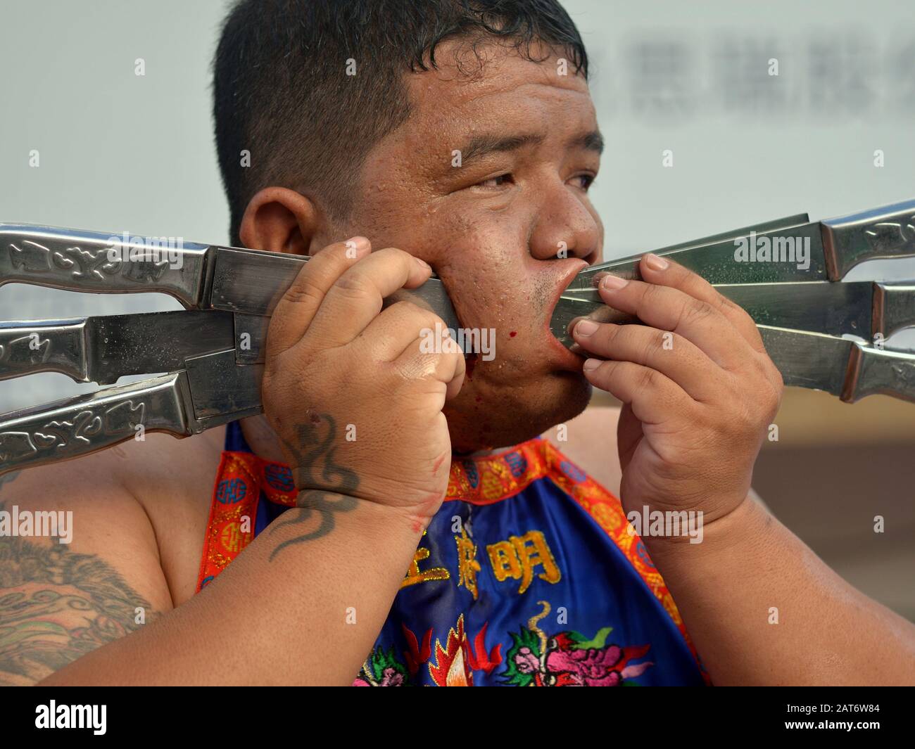 Der thailändische Taoist Devotee (mah Song, Masong) pierst seine rechte Wange mit sechs Messern während des Phuket Vegetarian Festivals. Stockfoto