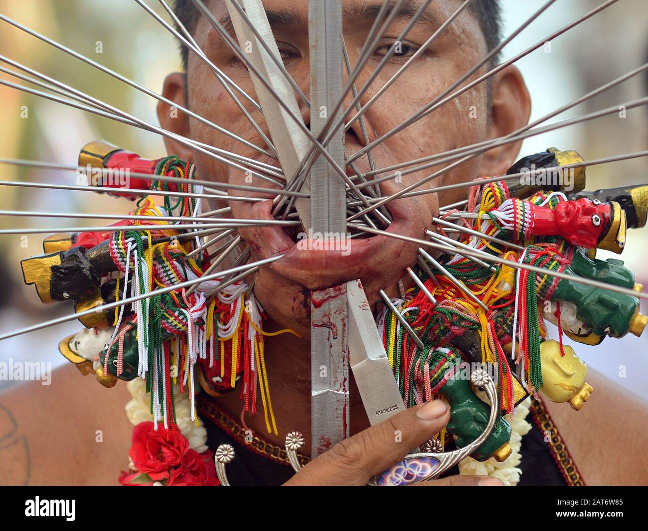 Der thailändische Taoist, der Anhänger ist, durchstößt seine Wangen und Unterlippe mit verzierten Stahlstiften/Spiegeln und zwei Schwertern während des Vegetarierfestivals in Phuket. Stockfoto