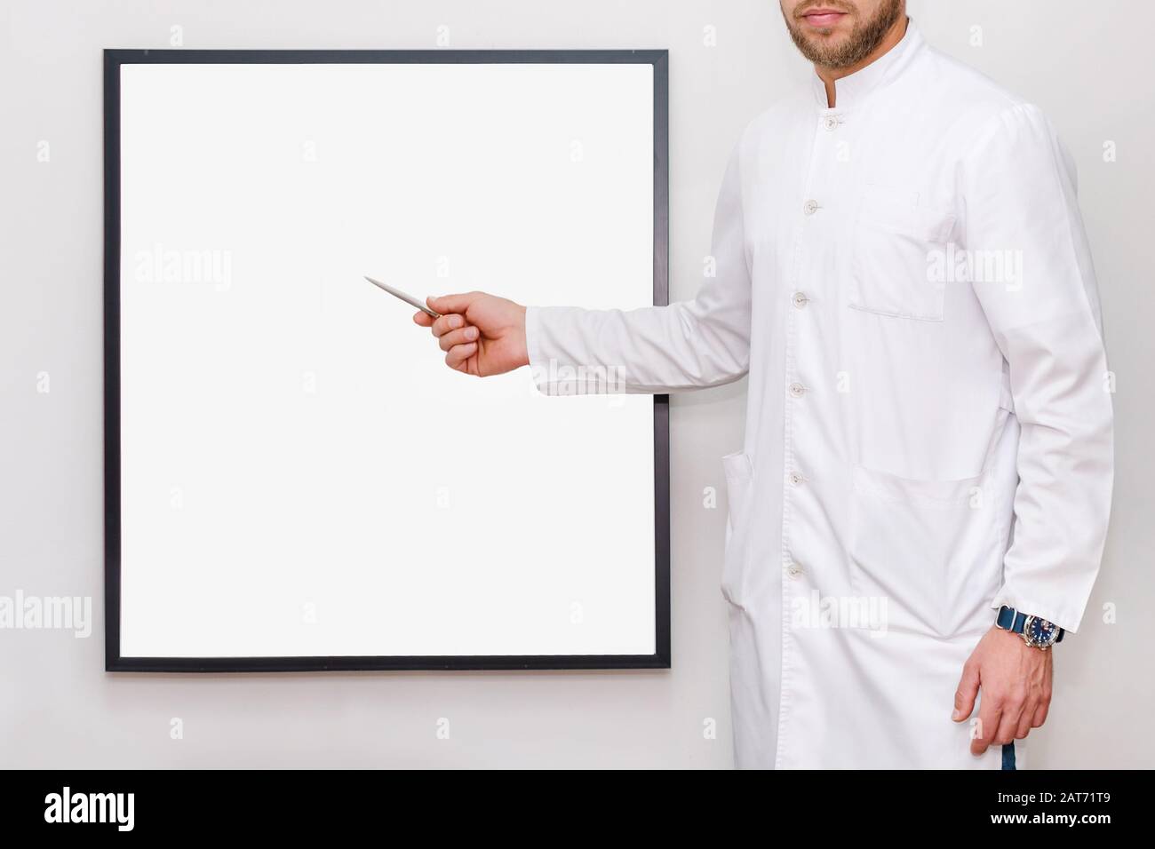 Mann in weißer Uniform, der auf einen Bilderrahmen oder ein Poster zeigt, um sich zu verspotten. Arzt oder Küchenchef zeigt leeren Rahmen, Medikamente, Geschäfte und Werbung Stockfoto