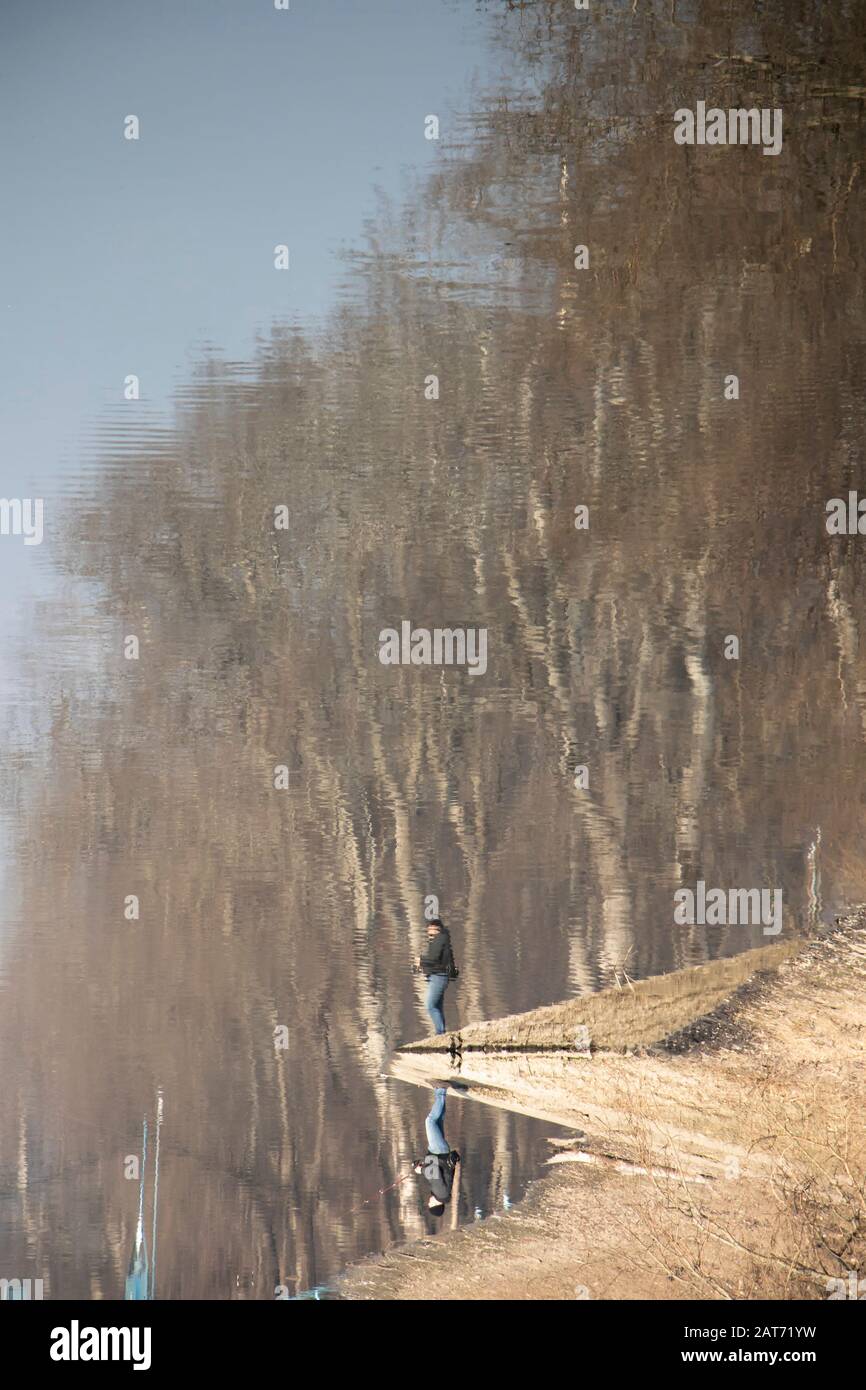 Verschwommene Silhouettenreflexion einer Person und eines Waldes in Flusswässern an einem sonnigen Tag Stockfoto