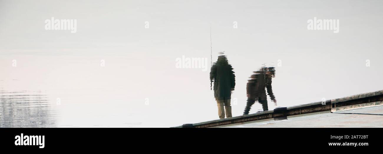 Verschwommene Silhouettenreflexion im Wasser von zwei Menschen, die auf einem Flussdock stehen, angeln Stockfoto