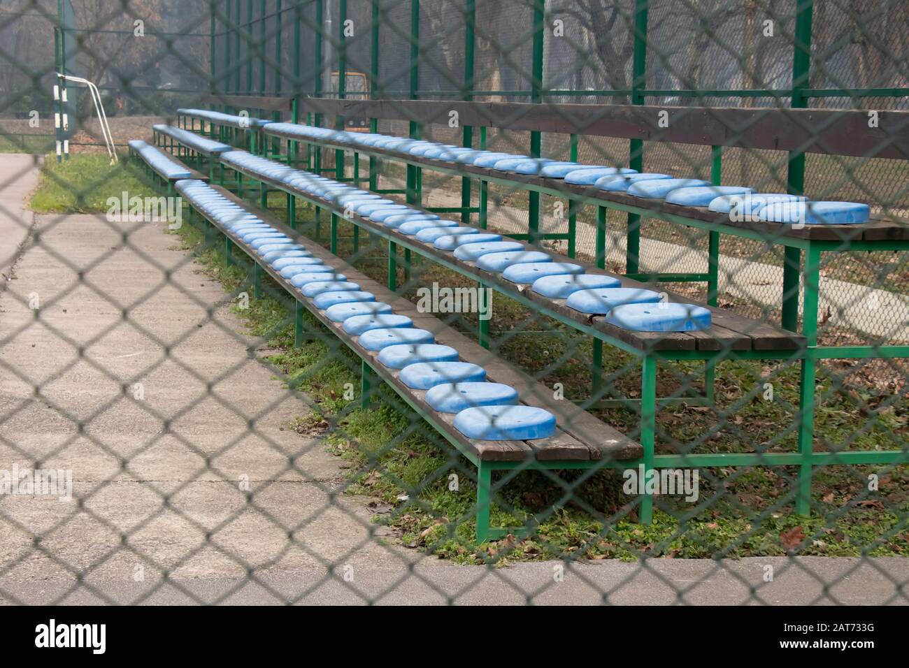 Tribüne mit blauen Kunststoffsitzen im kleinen Stadion hinter dem Drahtzaun Stockfoto