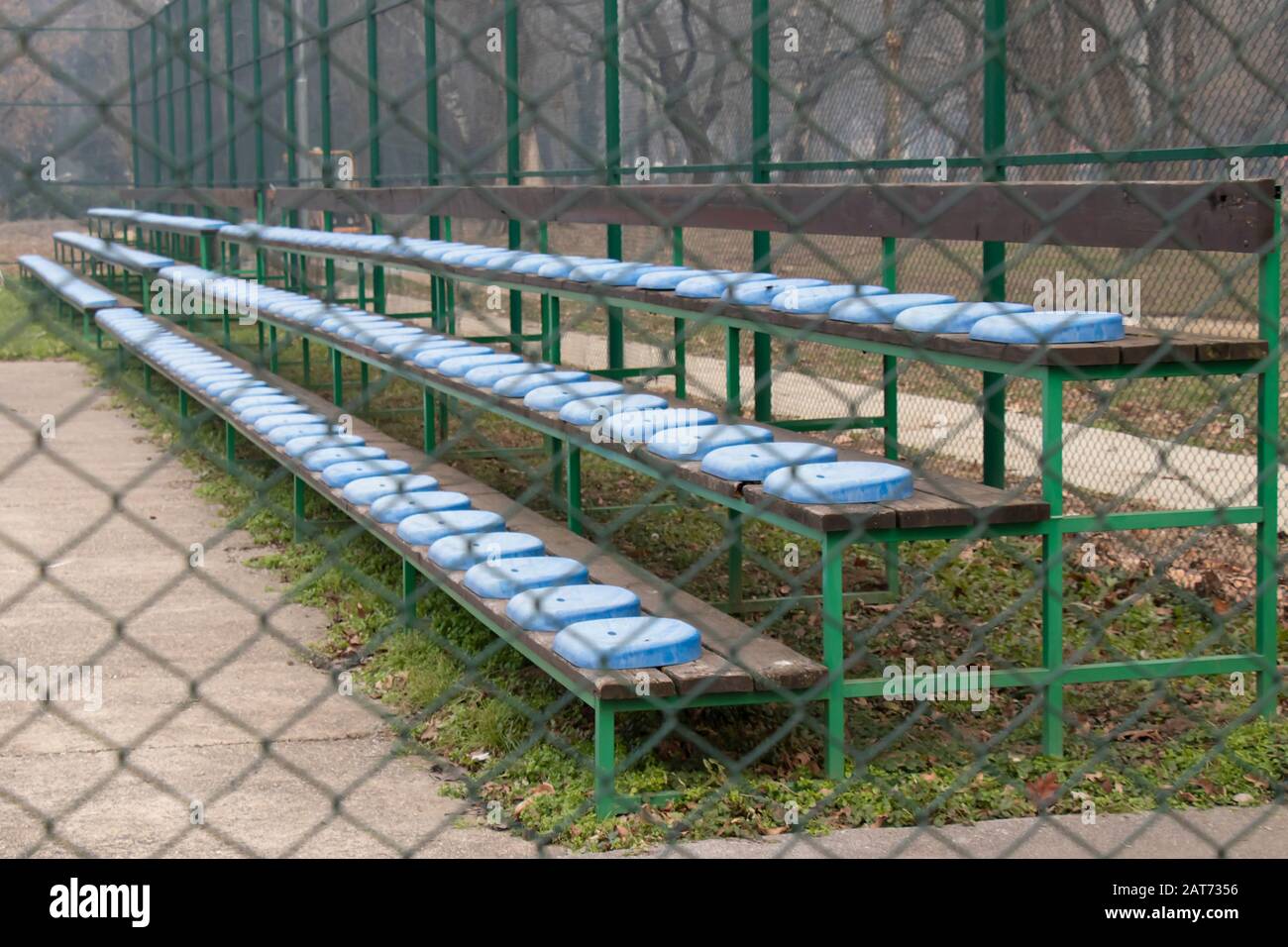 Tribüne mit blauen Kunststoffsitzen im kleinen Stadion hinter dem Drahtzaun Stockfoto