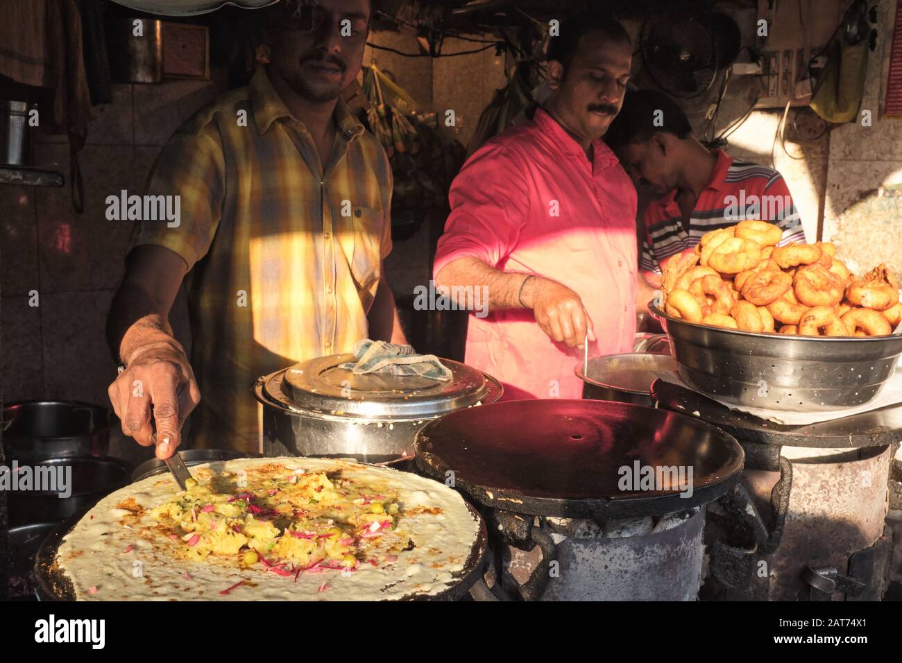 An einem Lebensmittelstall in Mumbai, Indien, bereitet ein Koch Masala Dosa, ein beliebtes indisches Gericht, zu. Rechts: Eine Schüssel Vade/Vadas, ein weiterer beliebter Snack Stockfoto