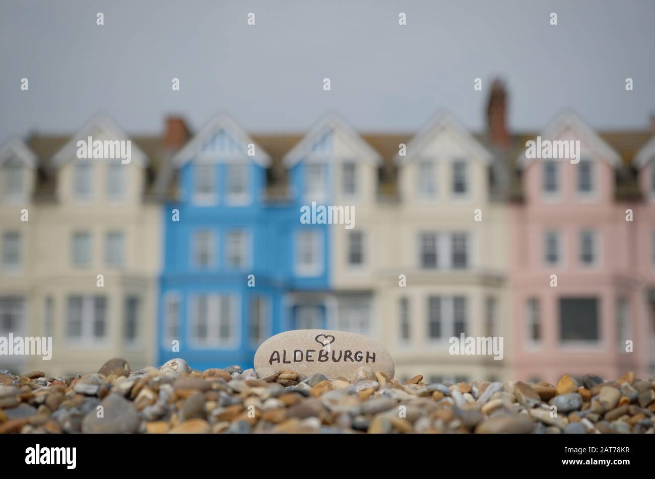Stein mit "Liebe (Herz) Aldeburgh", mit farbigen Häusern im Hintergrund. Stockfoto