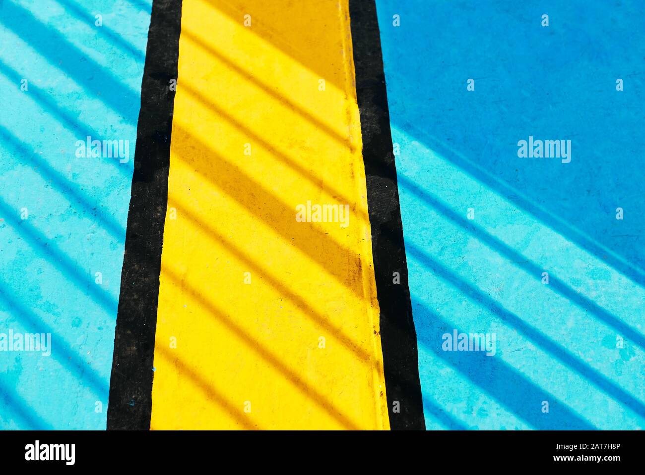 Diagonale Schatten, die auf einem hellen blauen Metallboden auf einem Schiff fallen. Darauf ist eine schwarze und gelbe Linie gemalt, die als Markierungen für Notausgänge dient. Stockfoto