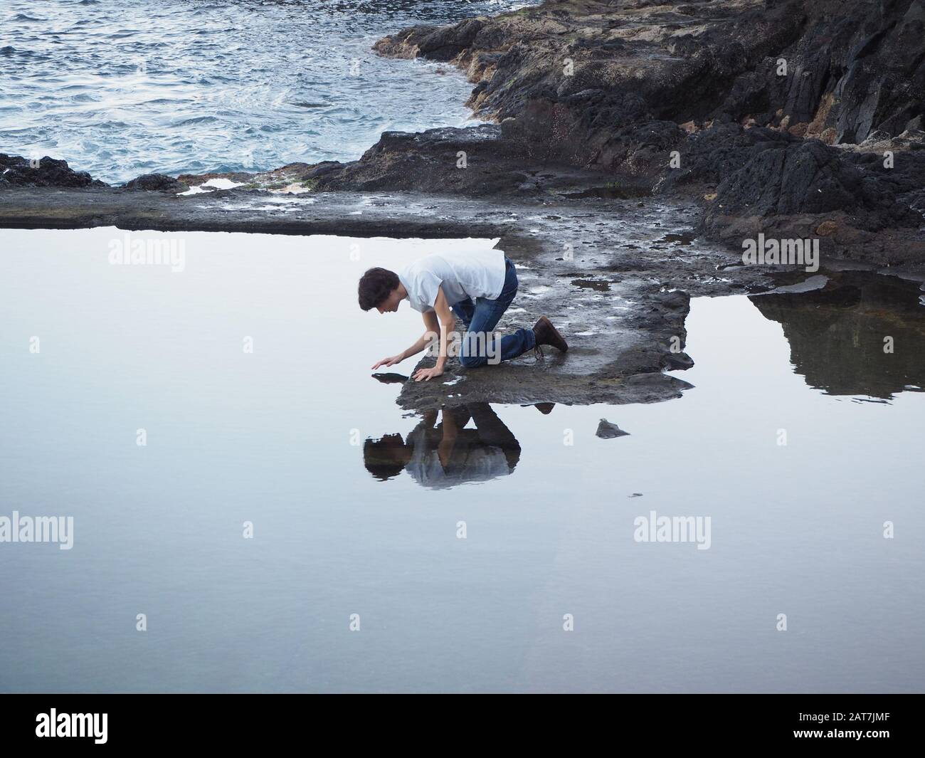 Junge, die das Wasser des Meeres berühren und sich wie der Narzissus-Mythos reflektieren Stockfoto