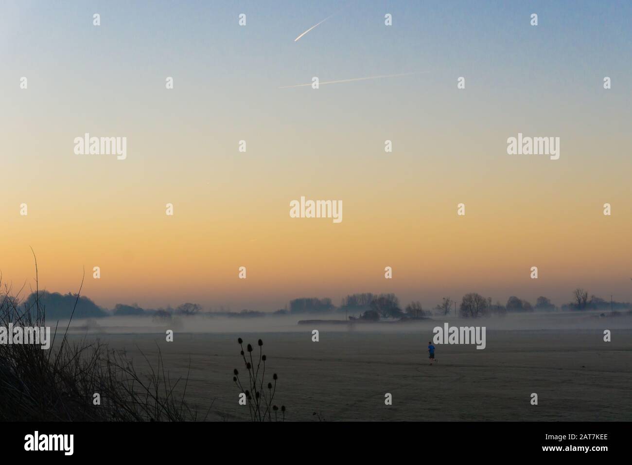 Person, die bei Sonnenaufgang über ein nebeliges Feld läuft, wobei der Mond zu sehen ist Stockfoto