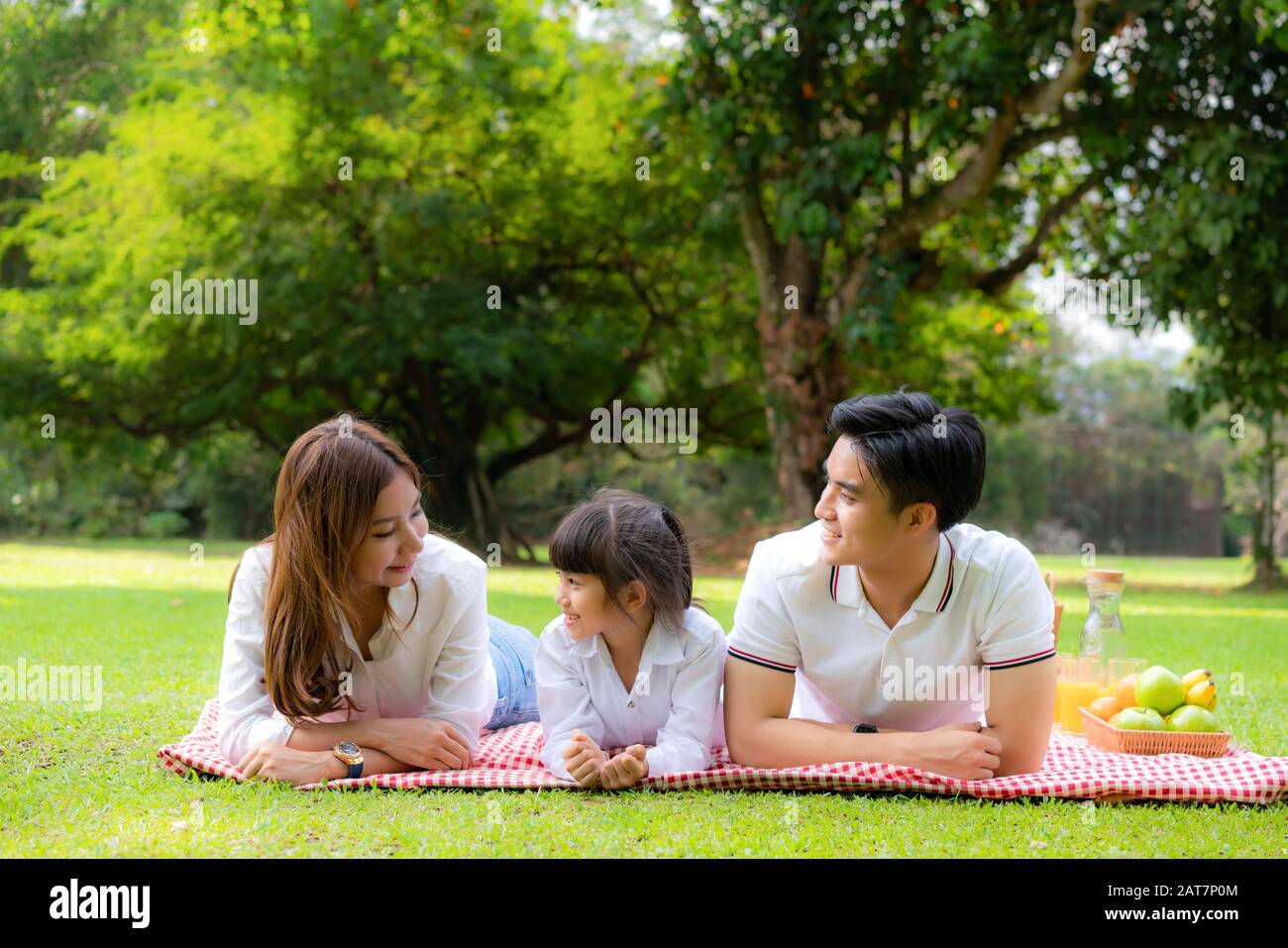 Asiatische Teenager Familie fröhlicher Urlaub Picknick-Moment im Park mit Vater, Mutter und Tochter liegen auf Matte und lächeln zu fröhlichen Urlaubszeiten zusammen Stockfoto