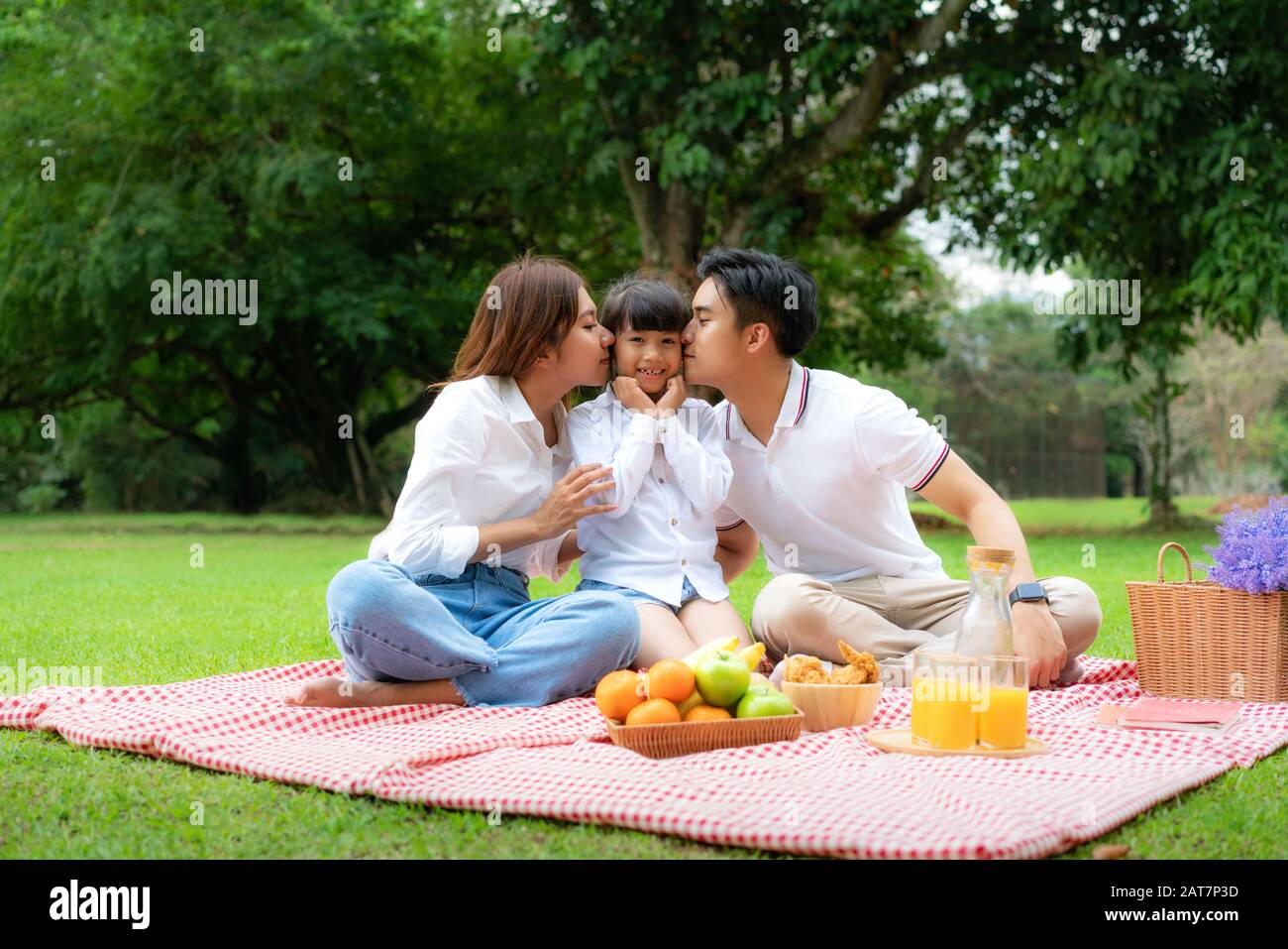 Asiatische Teenager Familie fröhlicher Urlaub Picknick-Moment im Park mit Vater, Mutter küssende Tochter mit Blick auf Kamera und Lächeln, um einen glücklichen Urlaub zu verbringen tim Stockfoto