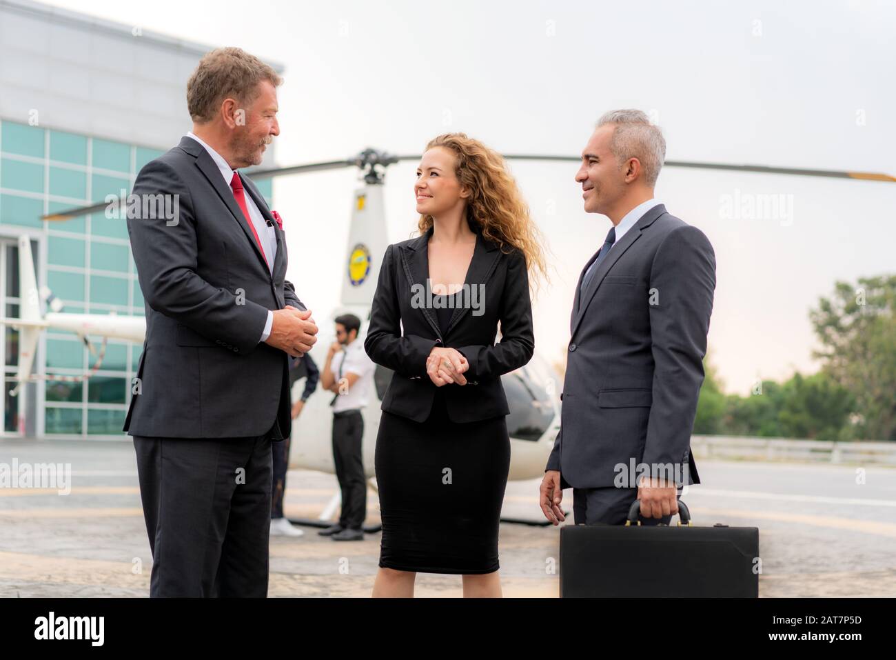 Drei Geschäftsfrau Und Geschäftsmann Im Gespräch mit Briefcase stehen in der Nähe eines Hubschraubers, wenn er mit helico am Hubschrauberlandeplatz am Flughafen ankommt Stockfoto