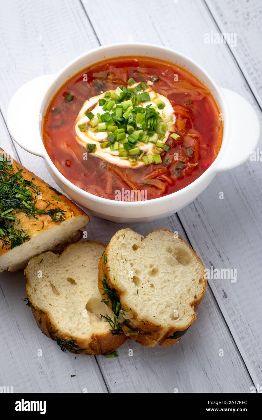 Russisches rotes Borscht mit saurer Sahne und Grüns in weißer Schüssel und Brotstücken auf Holzgrund, Tisch. Konzept der ukrainischen Küche Stockfoto