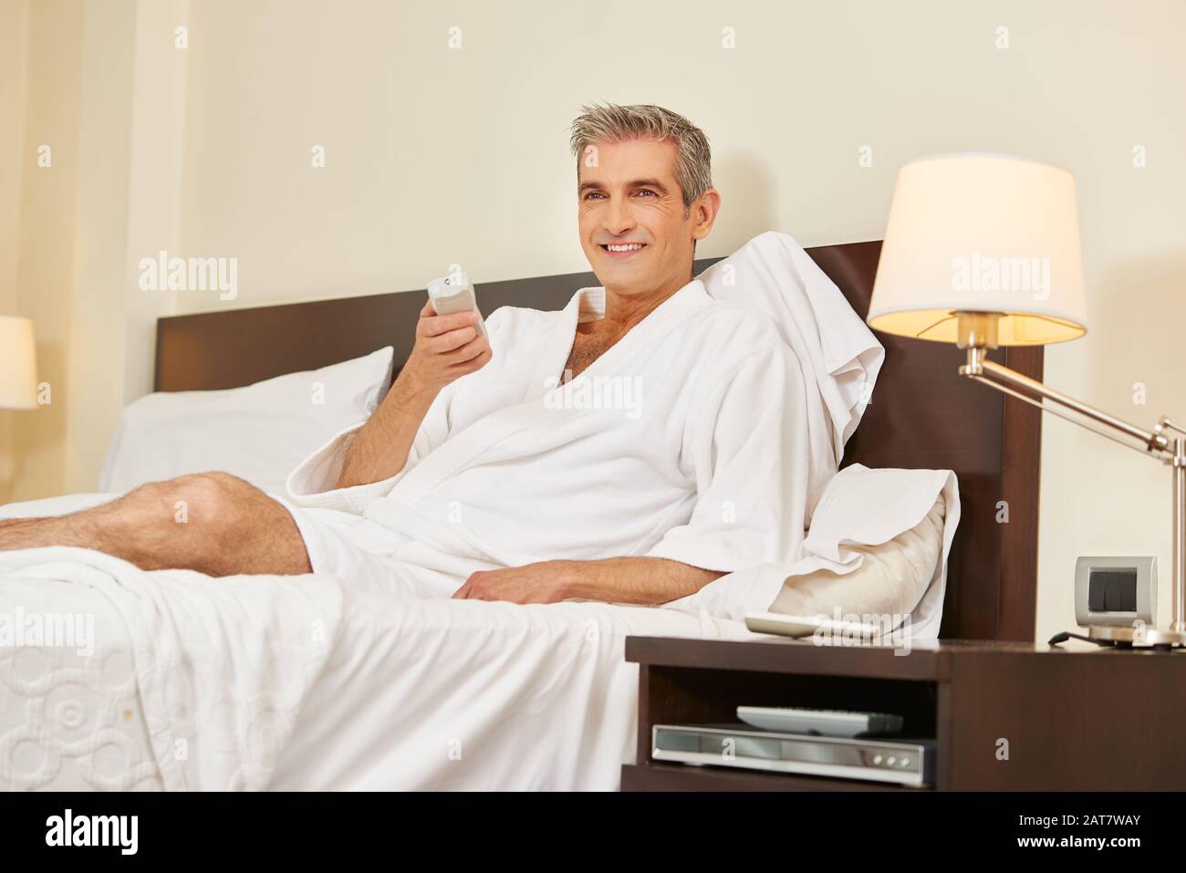 Lächelnder älterer Mann sieht im Hotelzimmer Fernsehen Stockfoto