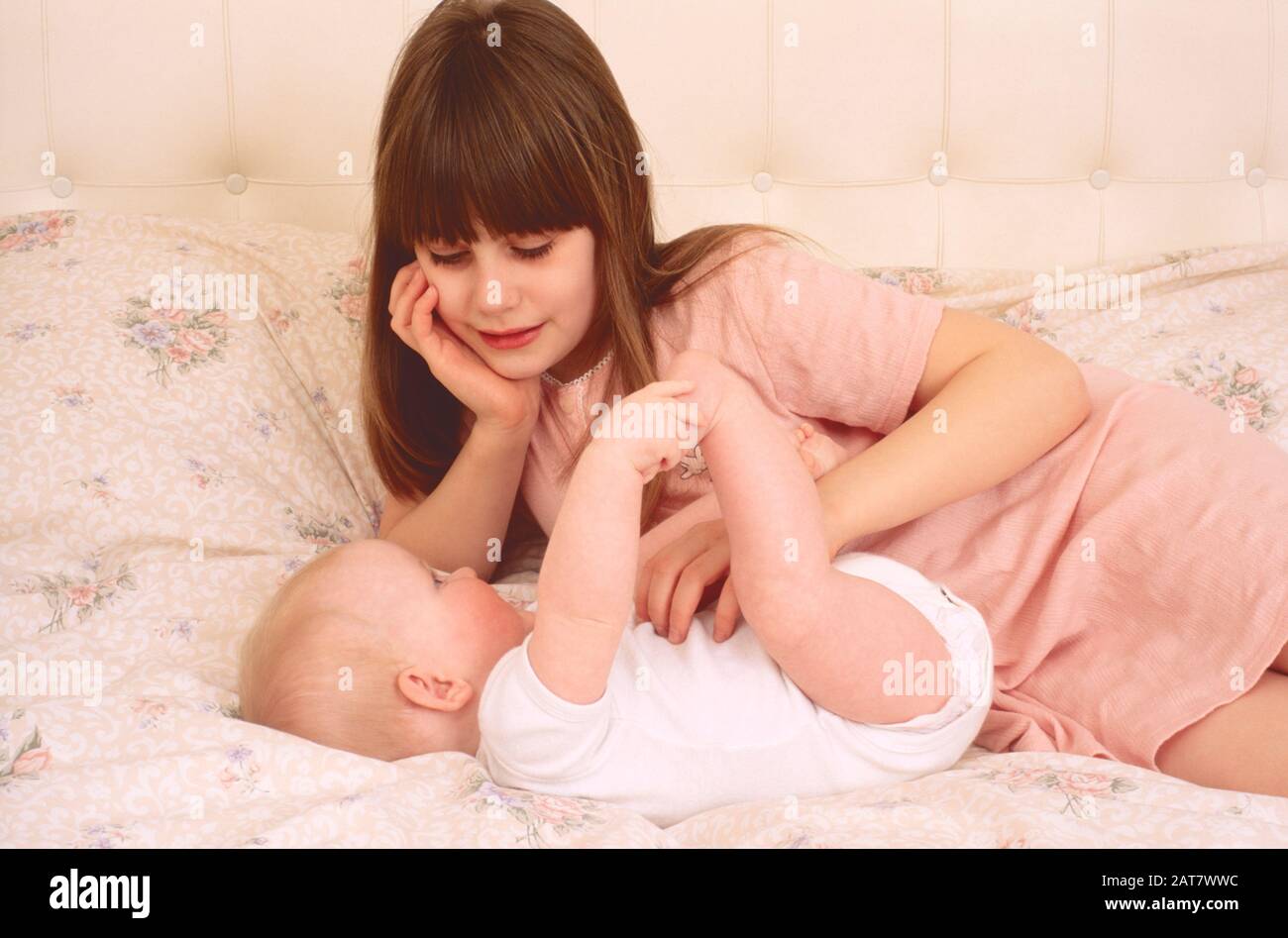 Mädchen, die auf ein Bett legen, das mit einem kleinen Baby spielt und dem Baby Liebe zeigt Stockfoto