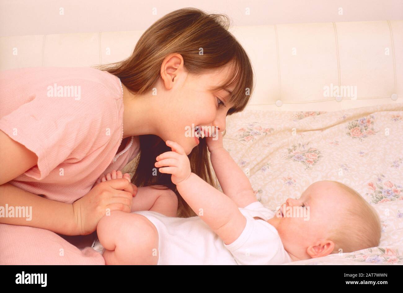 Mädchen, die auf ein Bett legen, das mit einem kleinen Baby spielt und dem Baby Liebe zeigt Stockfoto