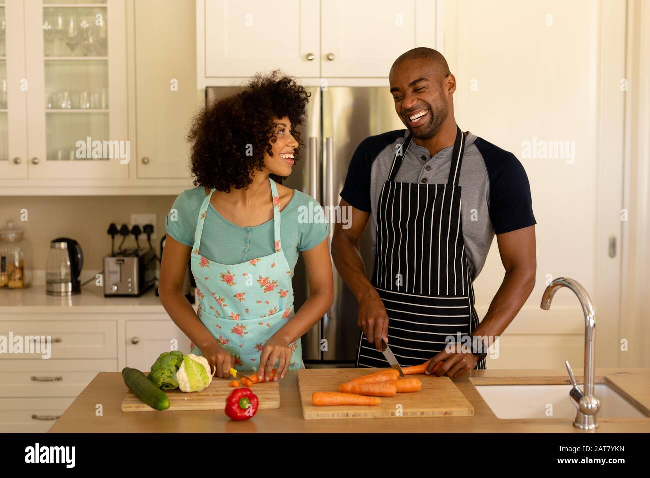 Fröhliches junges Paar, das in der Küche kocht und Schürze trägt Stockfoto