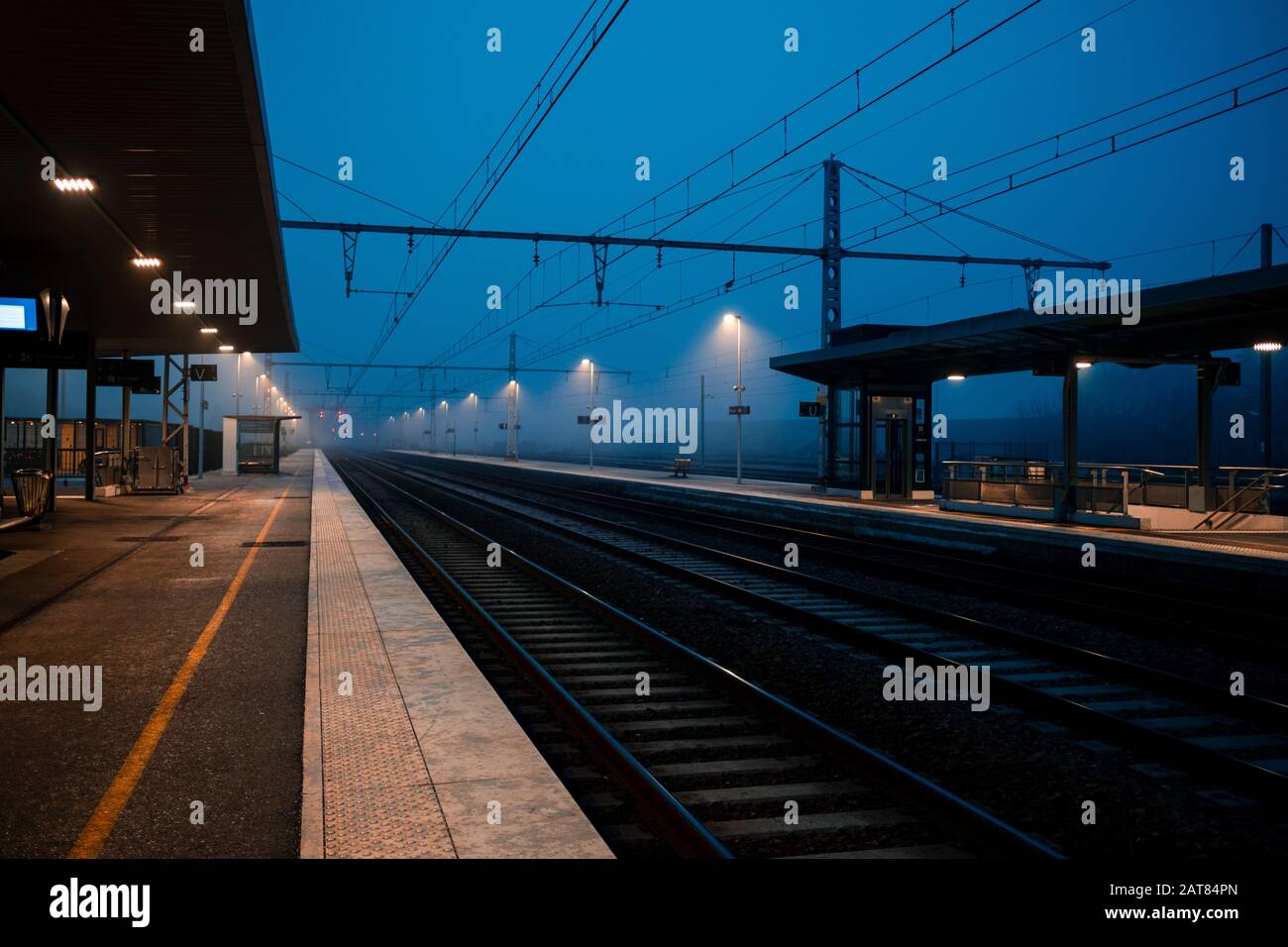 In der Abenddämmerung während der blauen Stunde siedelt sich ein dichter Nebel über einem leeren europäischen Bahnhof und Bahngleisen in Frankreich an. Stockfoto