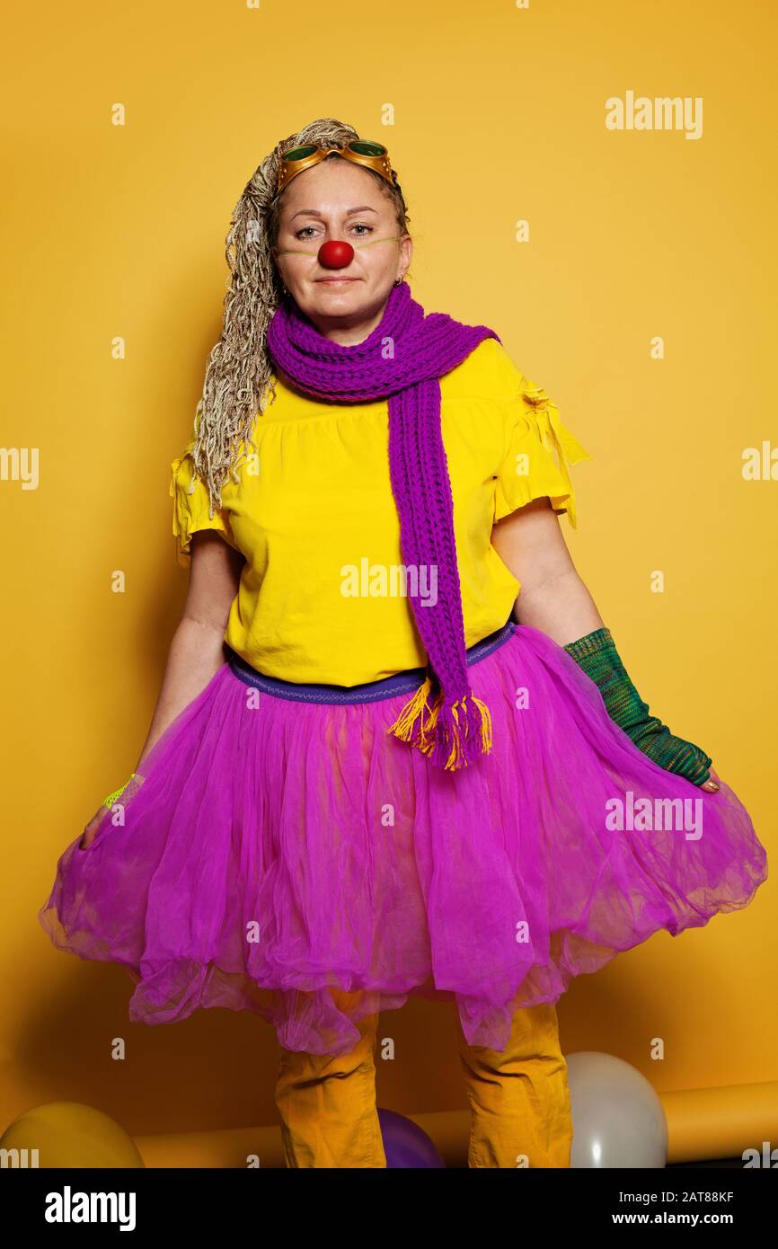 Frau mit farbenfrohem Clownkostüm auf leuchtend gelbem Hintergrund Stockfoto