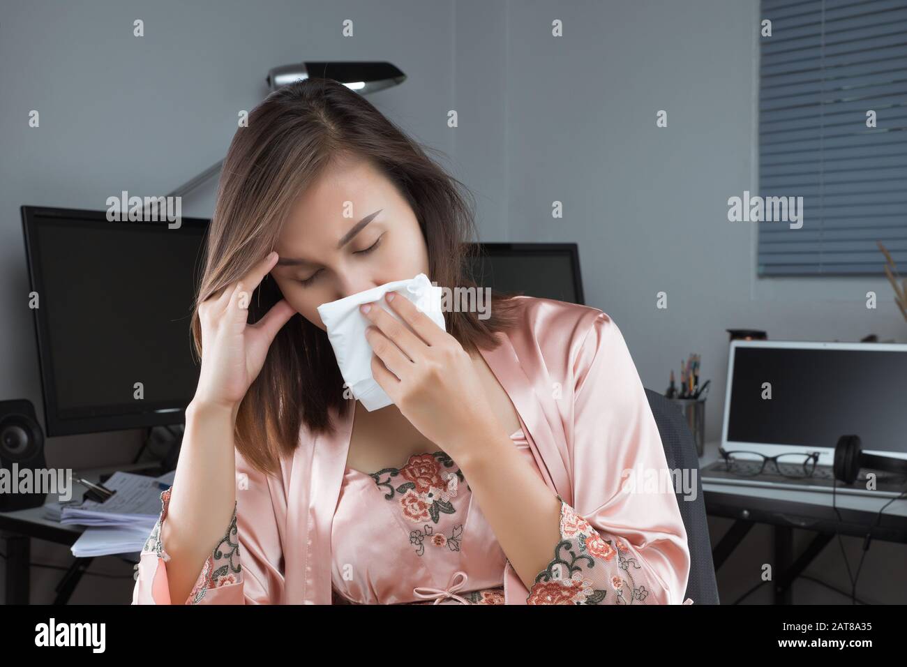 Asiatische Frauen in Satin nachtwäsche Unwohlsein und Niesen auf dem Schreibtisch zu Hause. Menschen erwischt Erkältung und Grippe. Stockfoto