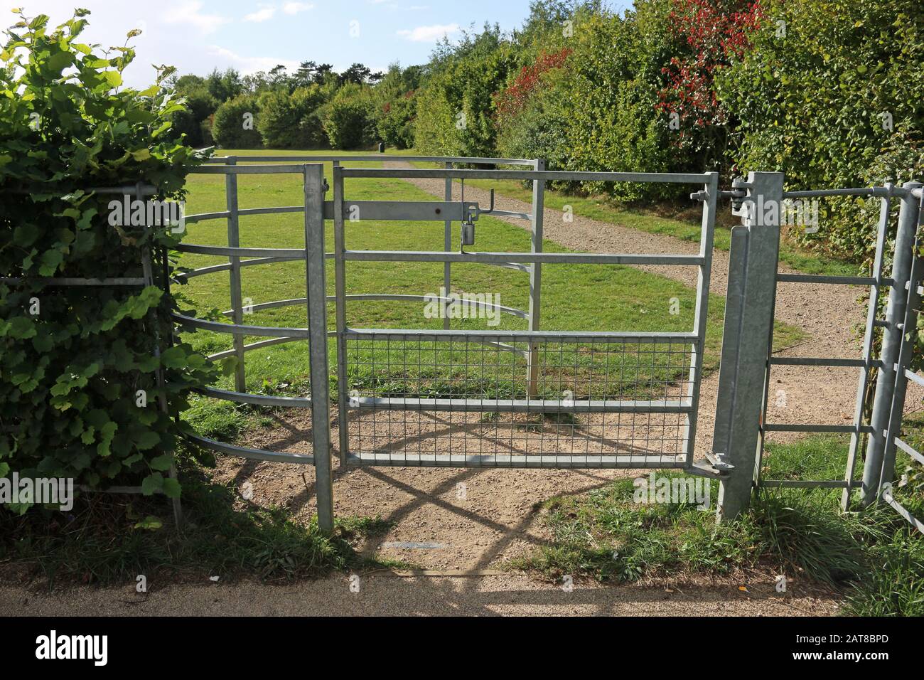 Verzinktes Metallküssentor am Parkeingang mit einem Kalkabschnitt und einer Rasenwiese und Bäumen im Hintergrund und Hecke links. Stockfoto