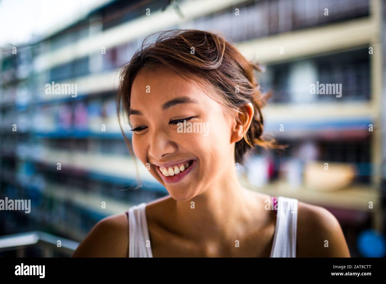 Porträt einer lächelnden jungen Frau mit braunen Haaren, die auf einem Balkon steht. Stockfoto